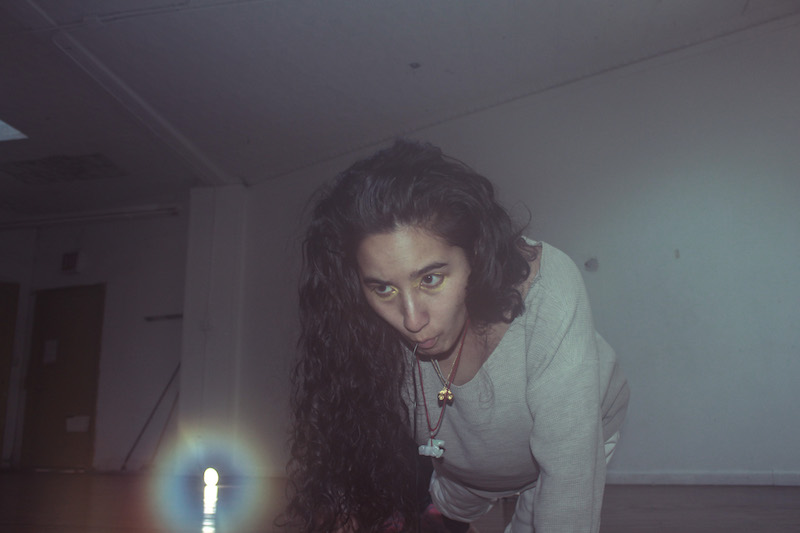 A person with long brown hair crawls towards a light on the floor.